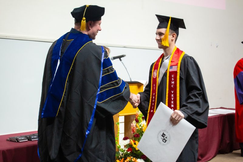 male student shakes hands with professor and receives diploma in full regailia